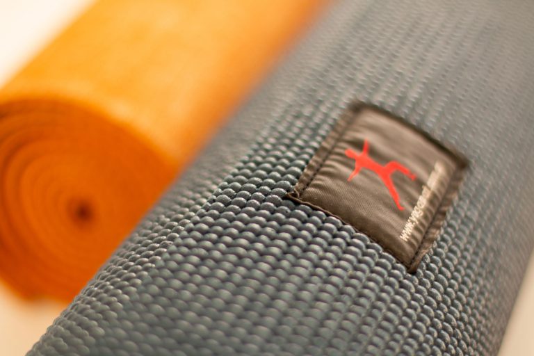 Primer plano de la textura y la etiqueta Yoga Mat en un mat gris, junto a un mat naranja enrollado