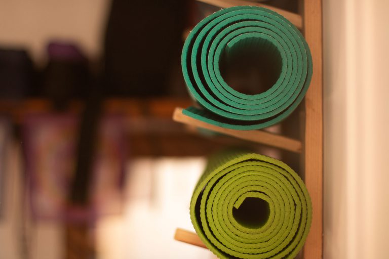 Dos mats de yoga verdes enrollados en un estante de madera