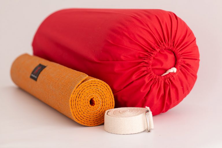 Mat de yoga naranja enrollado, bolso rojo y cinto blanco