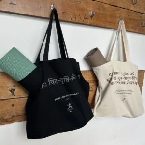 Mats de yoga guardados en bolsos de tela negro y crudo, colgados en una pared de madera